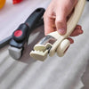 A hand is holding a light beige detachable cookware handle clip designed for pots and pans.