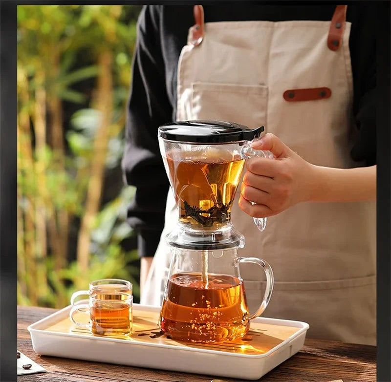 A hand pours brewed coffee from a glass dripper into a mug, set on a wooden tray.
