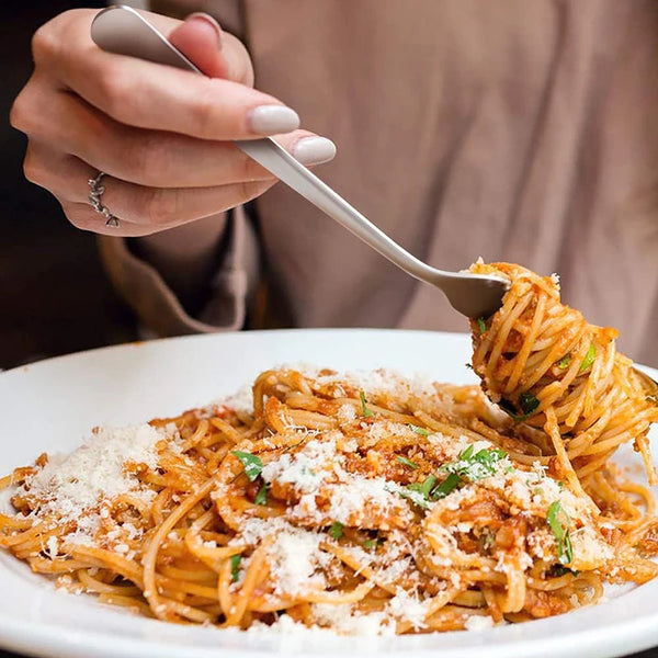 A hand holding a stainless steel dinner fork dipping spaghetti onto a white plate.