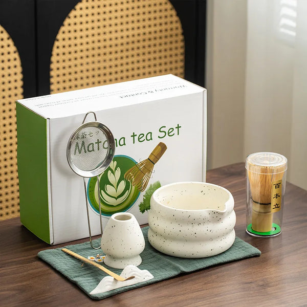 Weiße Box mit traditionellem japanischem Matcha-Tee-Set, Schneebesen und Schale, auf grünem Stoff.