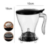 A clear glass pour over coffee dripper with a black lid and stand, shown next to dimension markers.