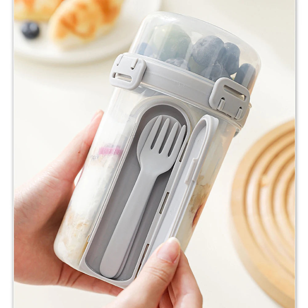 A hand holds a clear reusable container with a silicone lid, inside which are silverware for overnight oats and snacks.