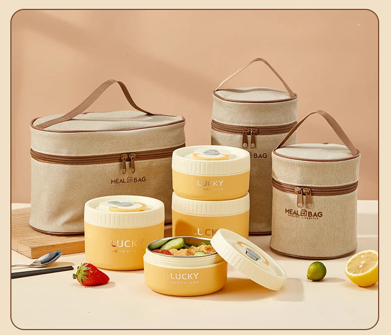 A set of portable stackable thermal lunch boxes in beige and yellow, shown with accessories on a light surface.