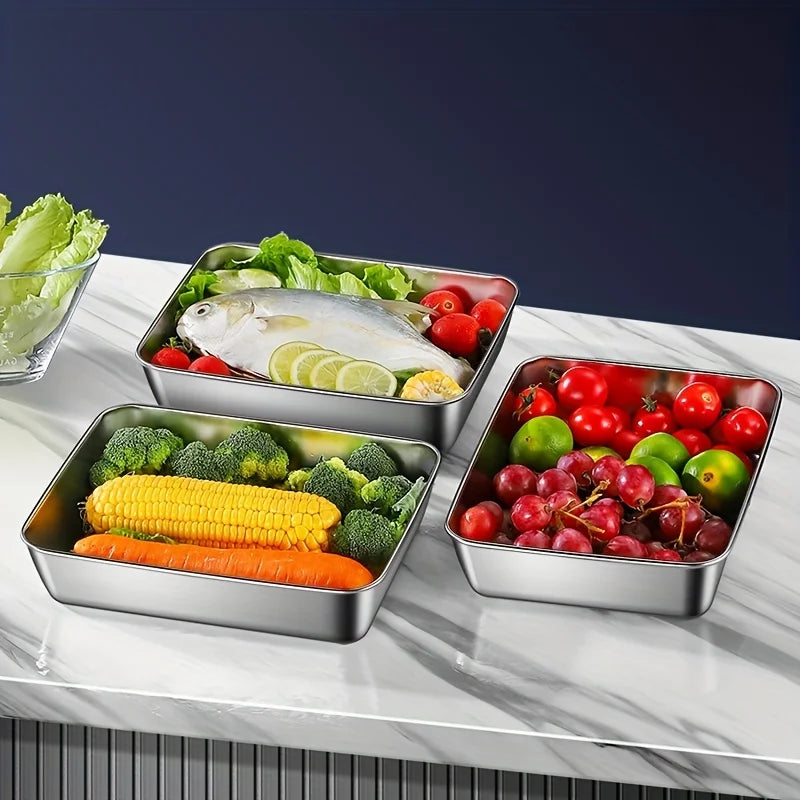 Stainless steel food storage containers filled with fresh vegetables and fish on a white marble surface