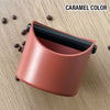 A terracotta-colored espresso knock box with a black interior sits on a wooden surface.