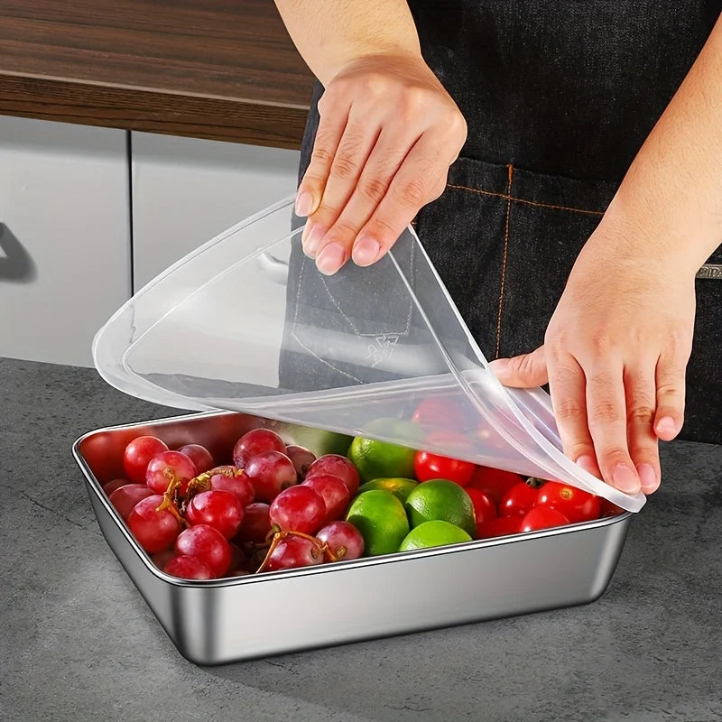 A hand is pouring a clear plastic bag filled with fresh tomatoes and limes into a stainless steel food storage container.