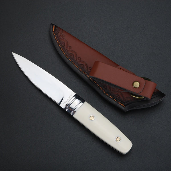 A compact M390 steel fixed blade knife with a silver blade and light-colored handle is shown resting on a dark surface.
