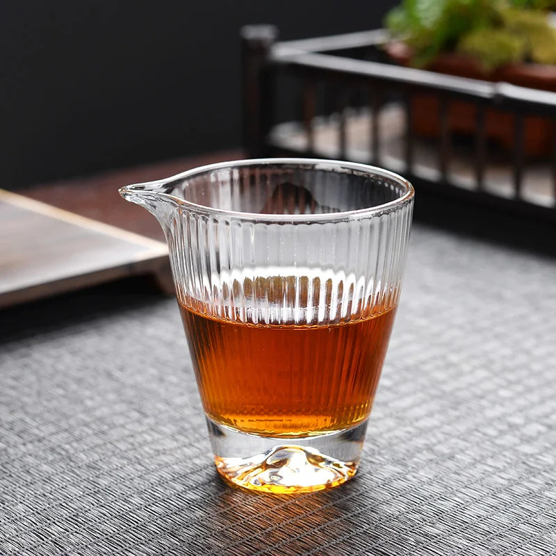 A clear glass teapot or cup filled with amber tea is placed on a dark surface.