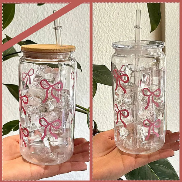 A clear glass tumbler filled with ice and decorated with pink bow patterns, held by a hand.