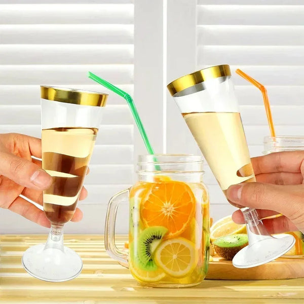 Hände halten klare, wiederverwendbare Champagnergläser mit gelblicher Flüssigkeit und orangefarbener Garnitur.