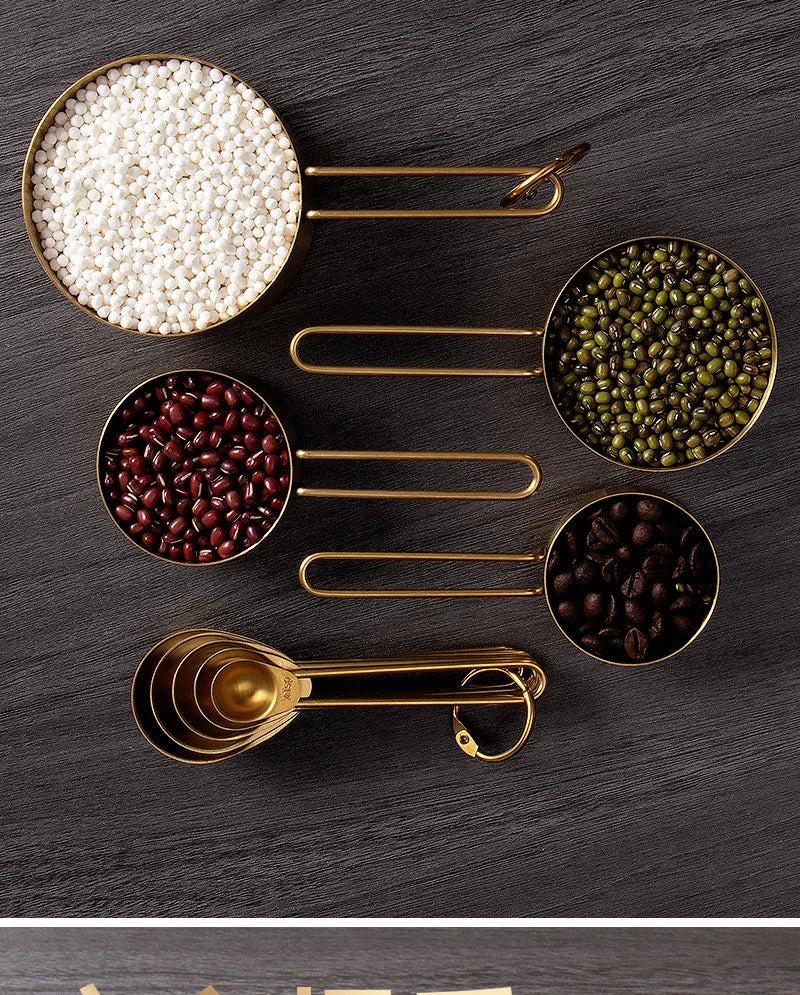 A set of gold-toned stainless steel measuring cups and spoons filled with various seeds and grains.