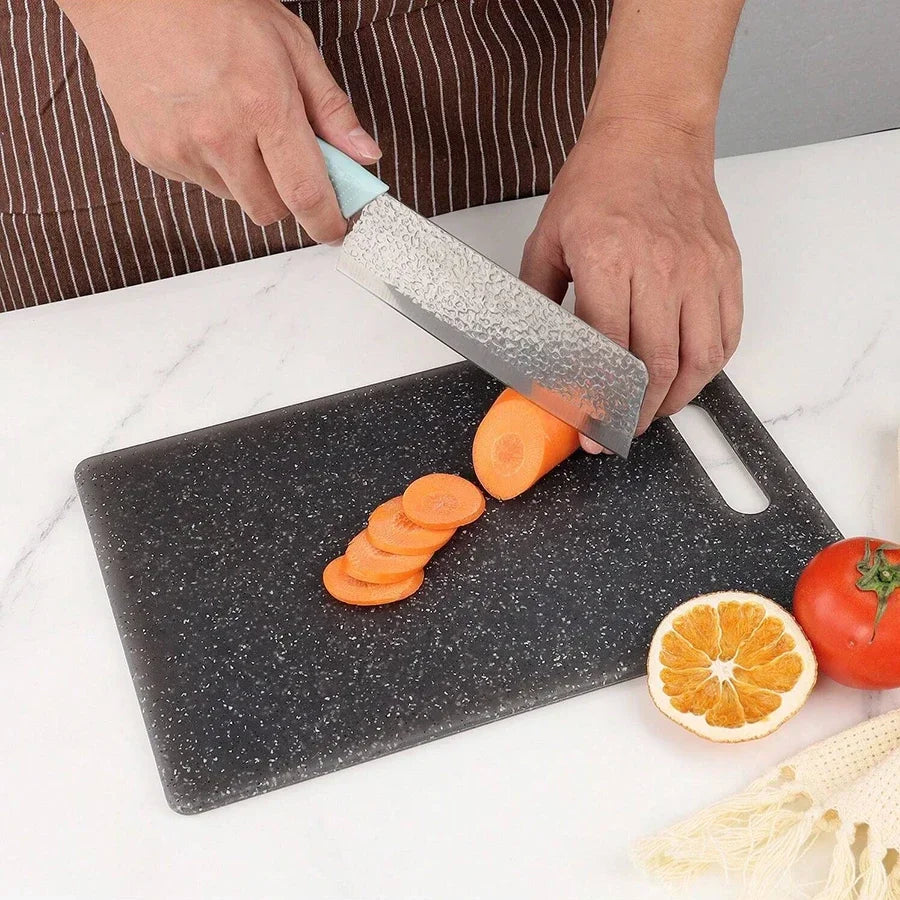 A hand is using a knife to slice orange segments on a dark marble texture cutting board.