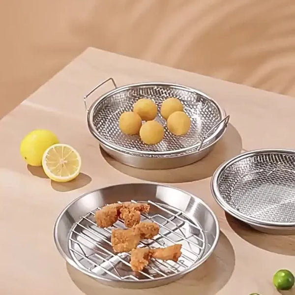 Edelstahl-Fritteusenrost mit Abtropfschale, der frittierte Hähnchenstücke und eine Zitrone auf einer hellen Oberfläche hält.