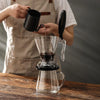 A person pours coffee into a glass carafe using a black pour over coffee dripper.