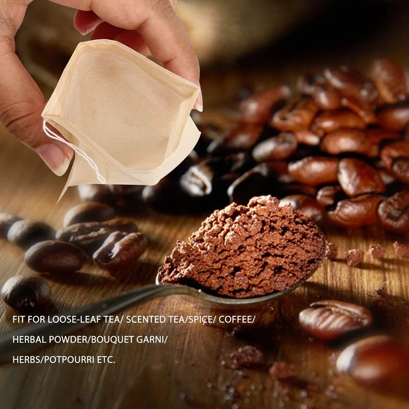A hand holds a light brown biodegradable tea filter bag above loose coffee beans and ground herbal powder.