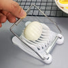 A hand is using a stainless steel egg slicer and divider to cut an egg, which is placed on a white plastic holder.