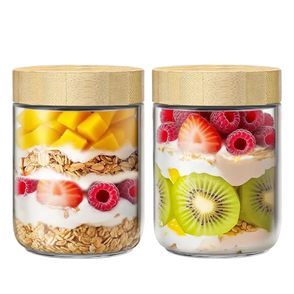 Two glass jars with bamboo lids filled with various fruits like mango, strawberries, raspberries, and kiwi.