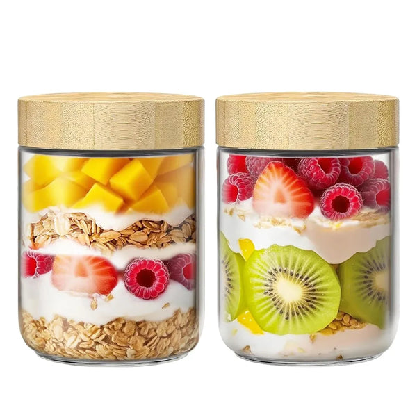 Two glass jars with bamboo lids filled with various fruits like mango, strawberries, raspberries, and kiwi.