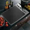 A silicone stove and cooktop protector mat is placed on a dark countertop next to cooking utensils and tomatoes.