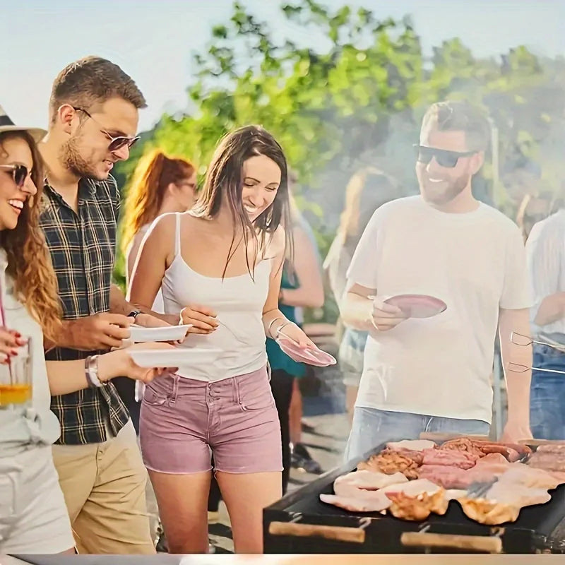 A man is preparing food on a black baking mat outdoors with several people nearby.