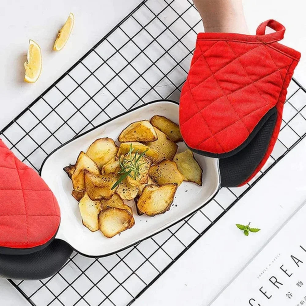 A pair of red heat resistant oven mitts with black non-slip silicone grips resting on a white plate filled with roasted potat