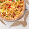 A pizza is shown on a wooden cutting board with a paper liner, featuring cheese, vegetables, and crispy toppings.
