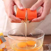 Hands are using a portable egg shell opener and separator tool to crack an egg in a glass bowl.