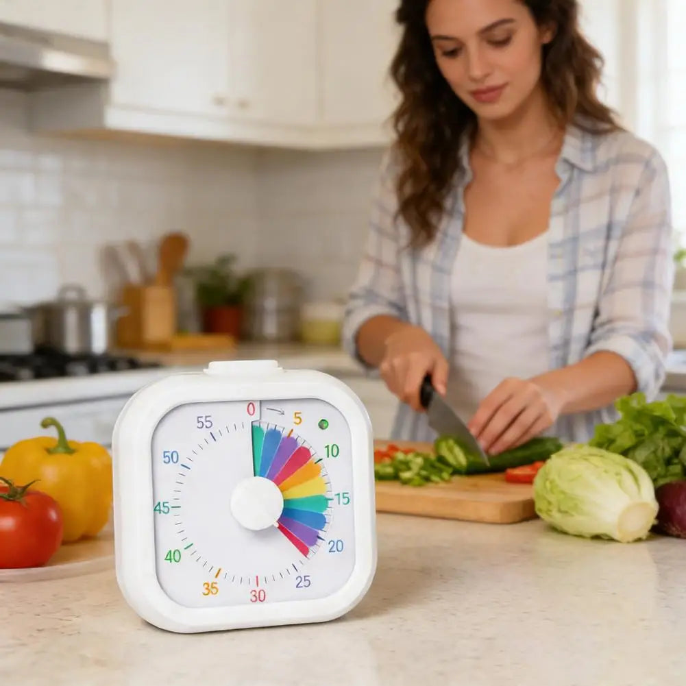 A white rainbow visual timer is placed on a kitchen counter next to fresh vegetables being cut by a woman.