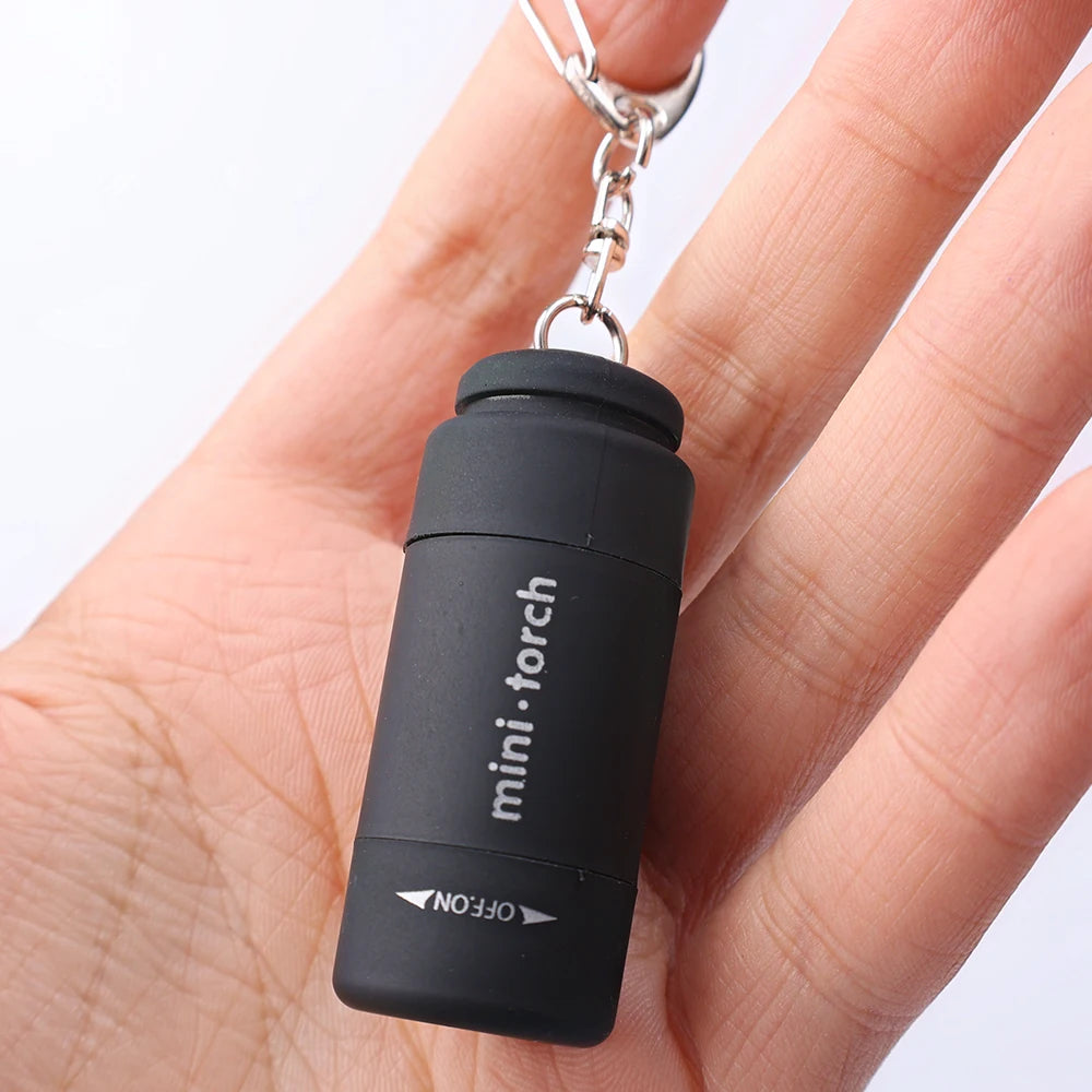 A hand holds a black mini-torch flashlight keychain with a silver clip.