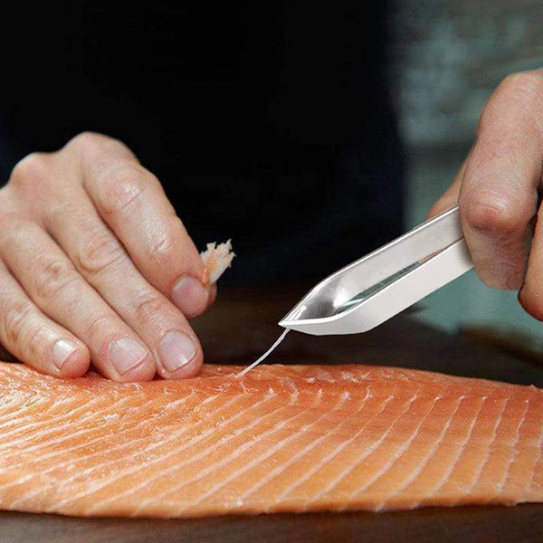 Eine Hand benutzt ein professionelles Edelstahl-Fischskalentool, um Schuppen von rohem Lachs zu entfernen.