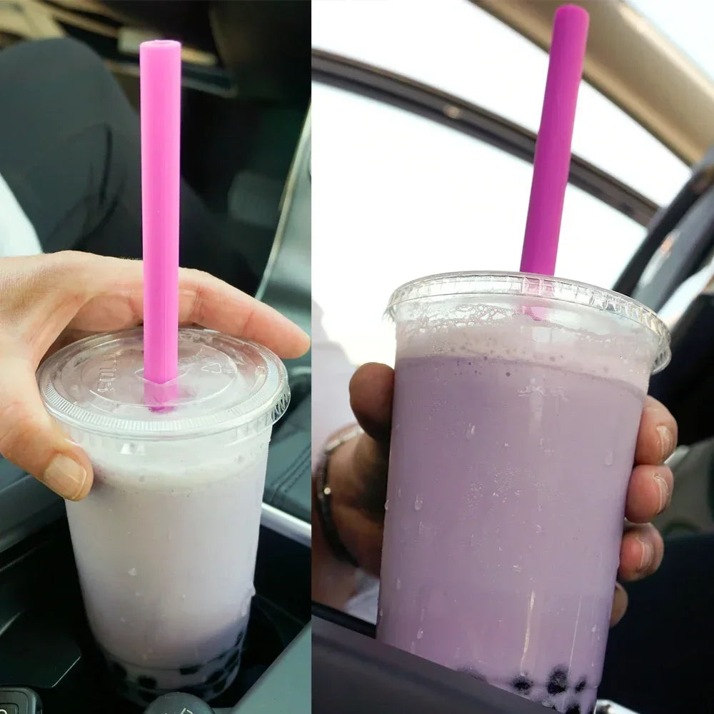 A hand holds a purple smoothie in a clear plastic cup with a pink straw, set against a car interior background.