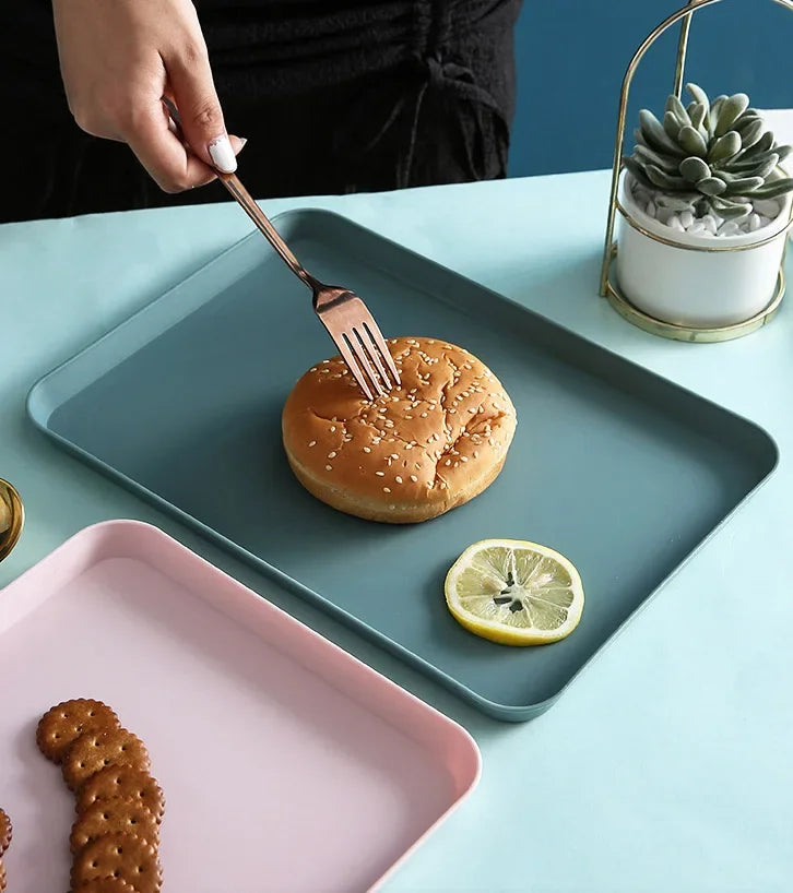 A silver fork is lifting a sesame seed bun from a dark gray serving tray, next to a lime and some cookies.