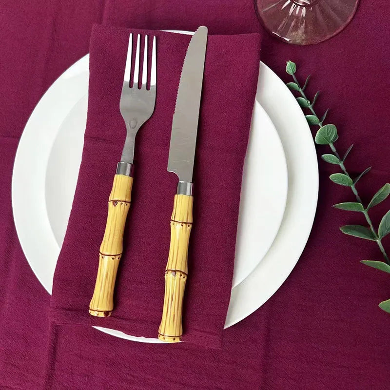A set of six burgundy cloth napkins placed on a white plate and a dark red tablecloth.