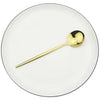 A gold-toned spoon resting on a white plate, part of a 6-piece Western stainless steel cutlery set.