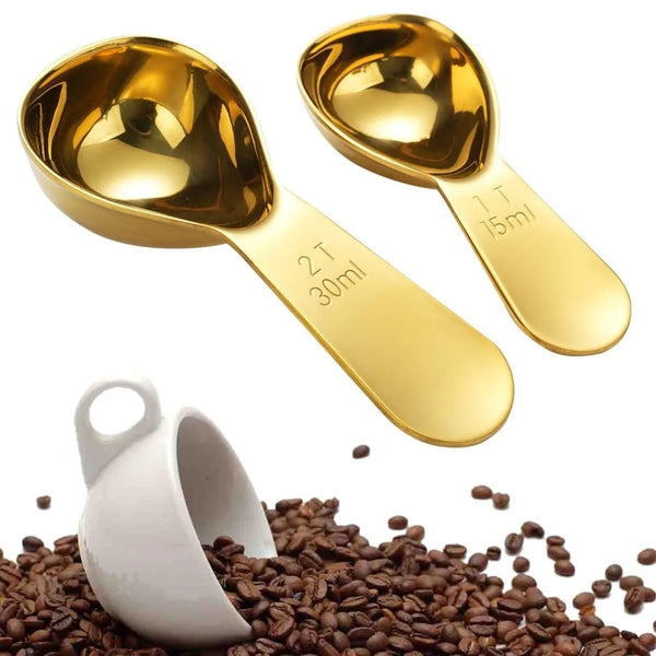 Eine goldfarbene Edelstahl-Kaffeelöffelpaar auf einem Haufen gerösteter Kaffeebohnen.