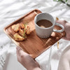A white mug of coffee sits on a wooden serving tray with some toast slices.