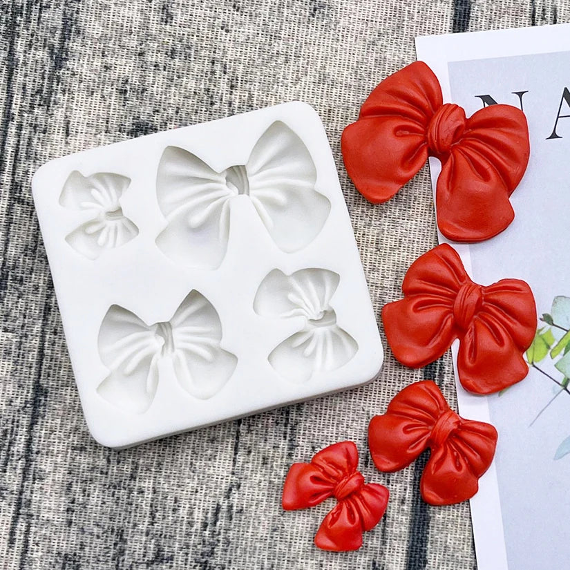 A set of silicone baking molds shaped like bows in a white tray next to several red fabric bows.