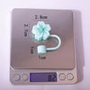 A silver measuring device shows a liquid level of 8.2 grams with a flower-shaped straw cap attached.