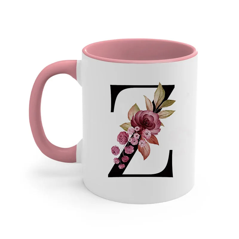 A pink coffee mug with a black monogram design featuring floral accents.