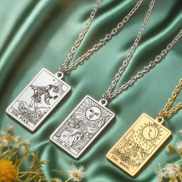 A silver tarot card necklace featuring images of The Fool, The Sun, and The Moon displayed on a green silk background.