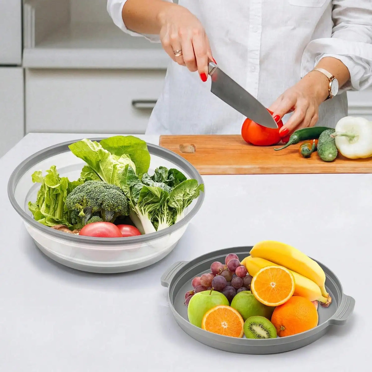 A person is using a knife to cut vegetables on a wooden board, with a bowl of fresh produce and fruit nearby.