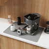 A black silicone induction cooker protector mat is placed on a white countertop next to an electric kettle and coffee pot.