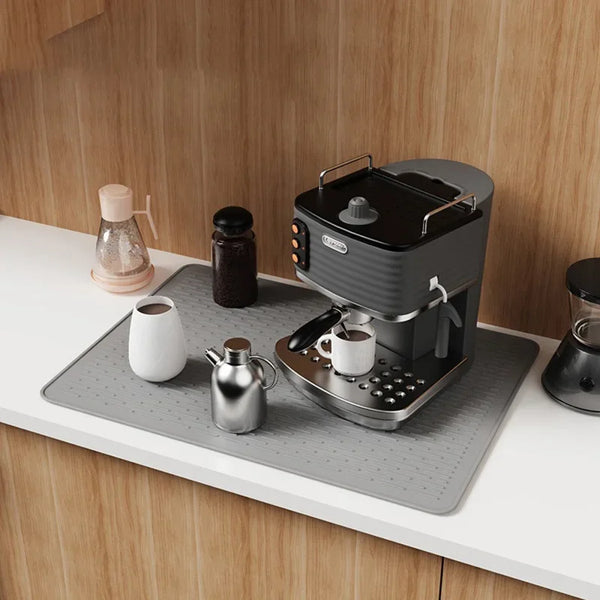 Ein schwarzer Silikon-Induktionskochschutzmatte auf einer weißen Arbeitsplatte neben einem Wasserkocher und einer Kaffeekanne