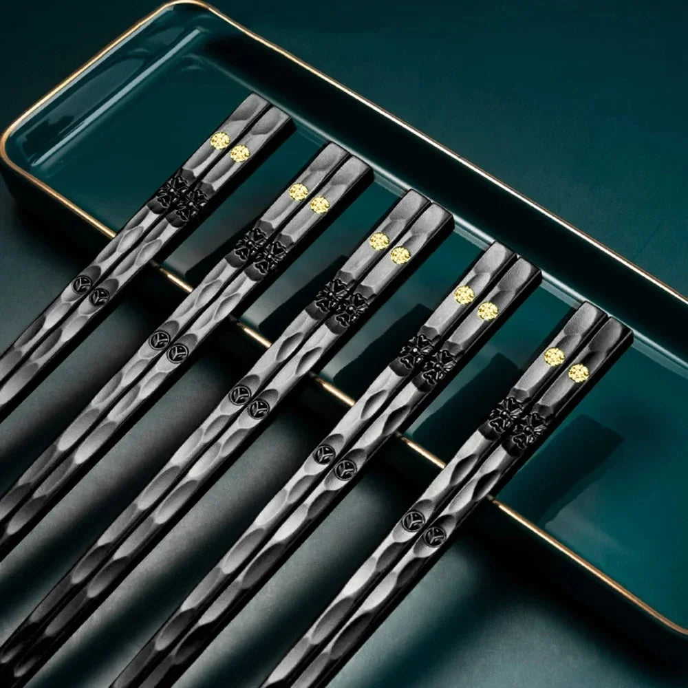 A set of five pairs of black metal chopsticks with gold accents resting on a teal serving tray.