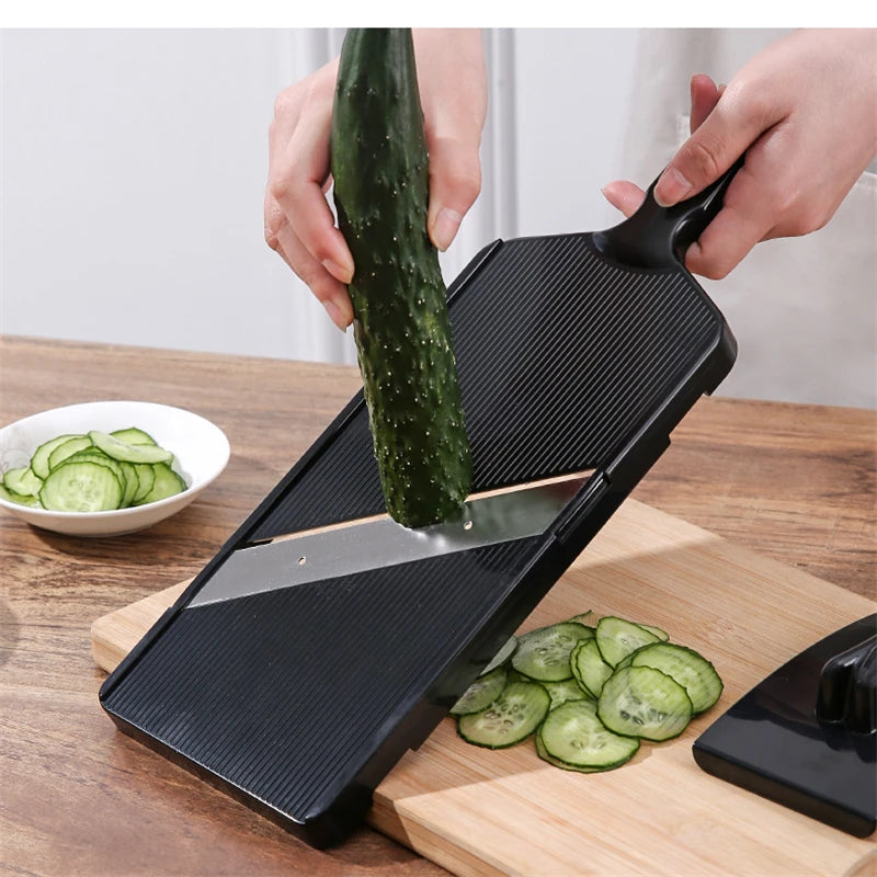 A hand is using a black vegetable grater tool to shred cucumber slices on a wooden cutting board.