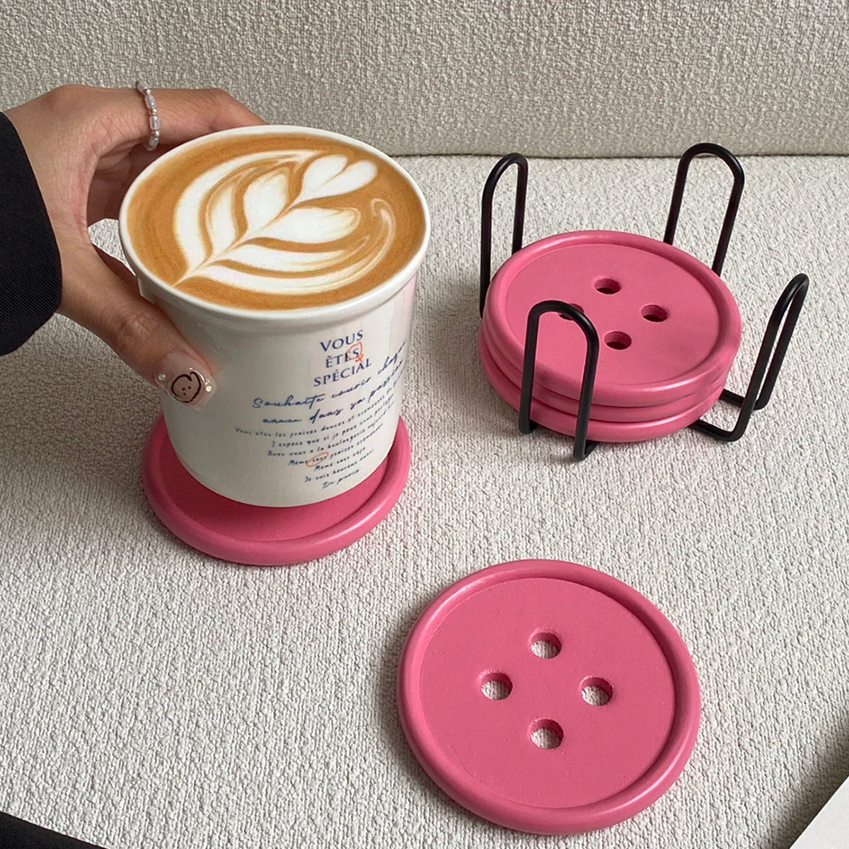 A pink wooden coaster set with an iron rack and a latte in a cup are displayed on a light surface.