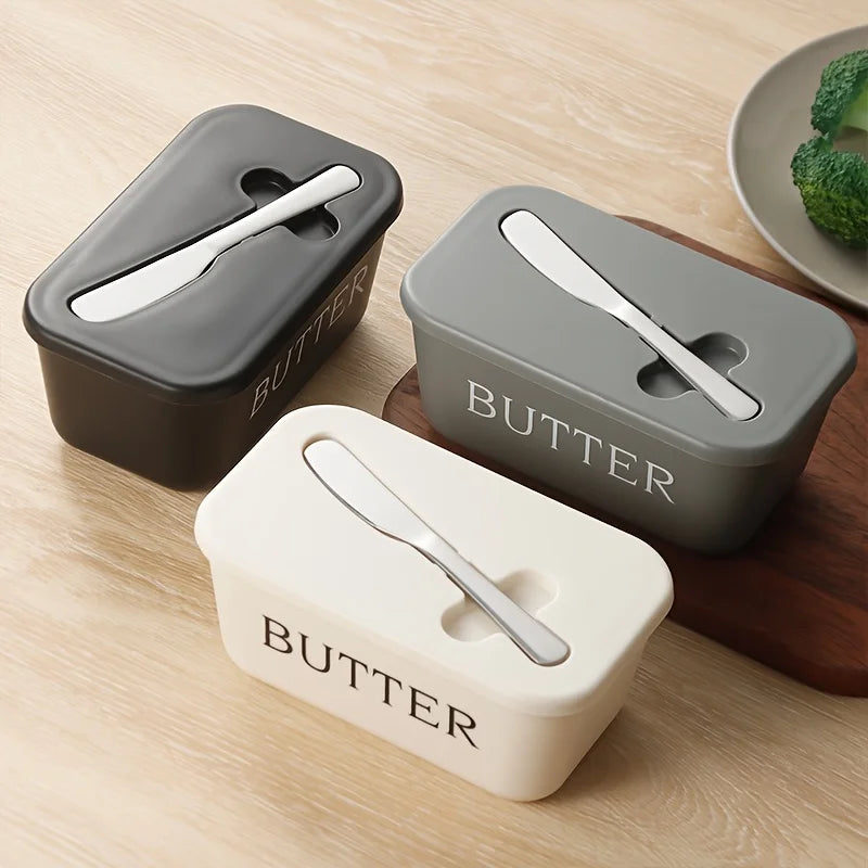 Three rectangular gray and white sealed butter storage containers with slicer knives resting on a wooden surface.