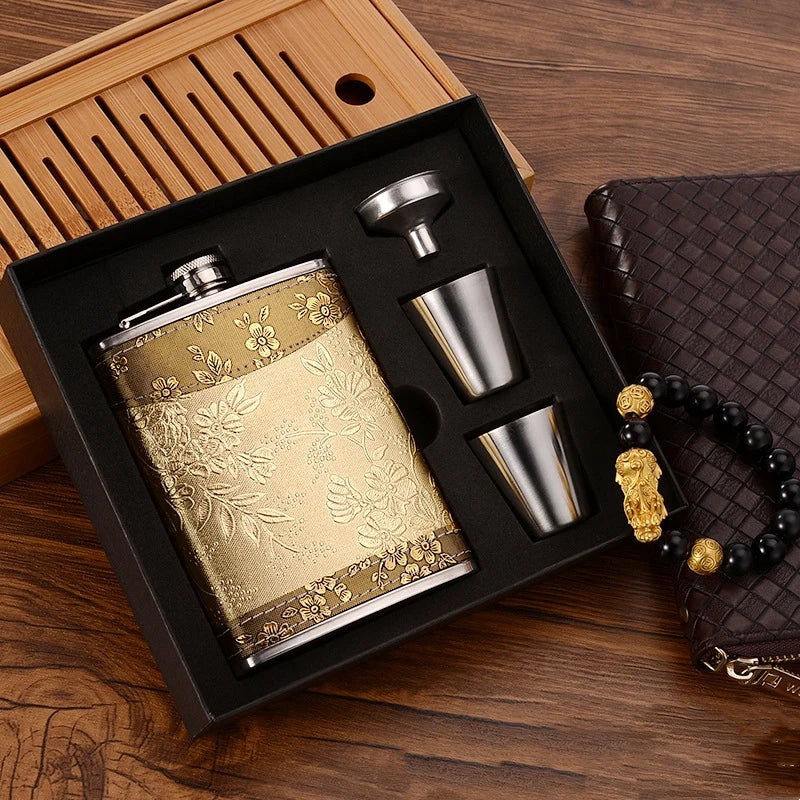 A portable stainless steel hip flask in gold and silver accents is displayed in a wooden box with matching metal accessories.