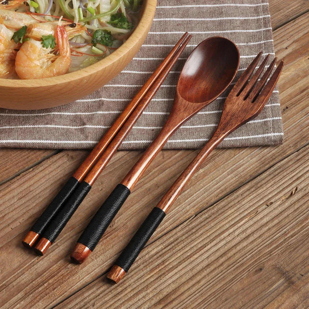 A set of natural wood dining utensils including a spoon, fork, knife, and chopsticks resting on a striped cloth.