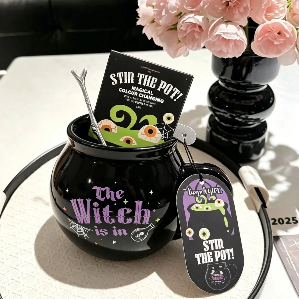 A black cauldron mug with a witch design and a tag reading Stir the Pot.